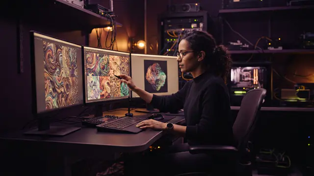 An AI researcher working at computer monitors displaying generative visuals